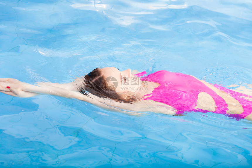 穿着粉红色泳衣在蓝池游的年轻女子在度假胜地游泳的年轻女子体育活动健康概念在游泳池的漂亮女子在游泳池图片