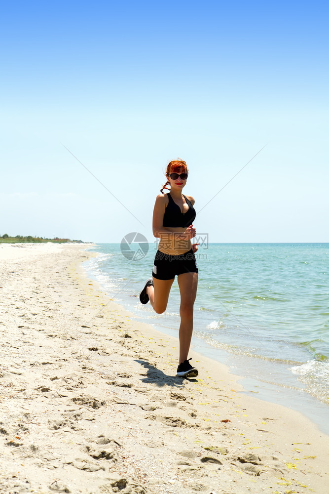 身穿运动服的年轻女孩在荒漠的海岸上慢跑图片