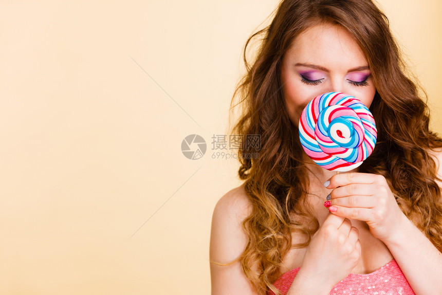 美女有色人种的双眼装着大棒糖遮住她的脸甜美食物和享受概念工作室拍到光亮女人拿着多彩的棒糖遮住脸图片