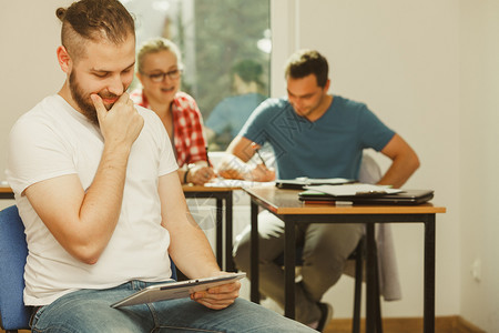 教育高中数字在线学习概念平板电脑的学生男孩坐在课堂上同班学面前的生图片