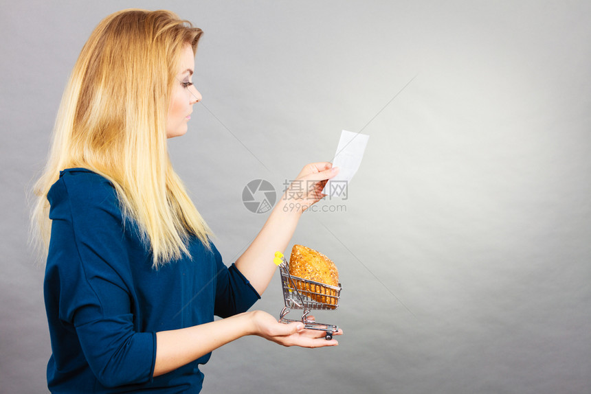 带着面包的快乐妇女拿着购物篮看收货单思考着价格图片