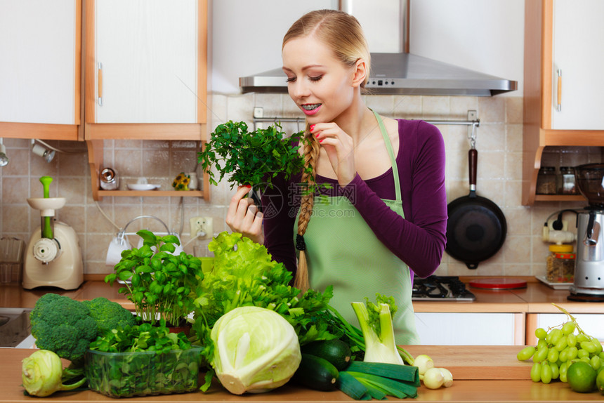 厨房里有许多绿叶蔬菜新鲜有机农产品的妇女在柜台上年轻家庭主妇手握着面纱健康饮食烹饪素饮和人的概念带绿色蔬菜的女家庭主妇在厨房里图片