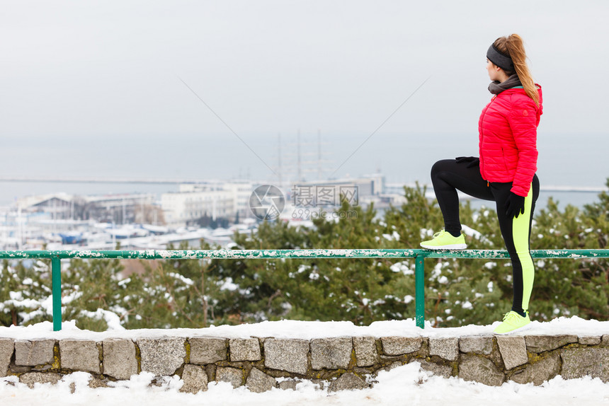 穿着温暖运动服的妇女冬季在户外伸展腿部运动背景的城市观全冬季穿着运动服的妇女冬季运动图片