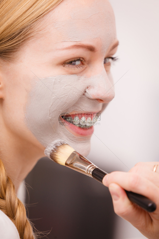 Skincare年轻女在脸上用刷灰泥面罩女照顾皮肤状况斯帕美容治疗女在脸上用刷灰泥面罩图片