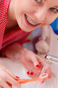有牙套的女孩拿着刷在自来水下洗刷口腔卫生图片