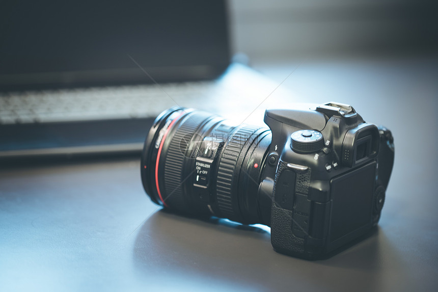 摄影师手上拿着一个专业相机手持远光镜头在模糊背景的笔记本电脑上图片
