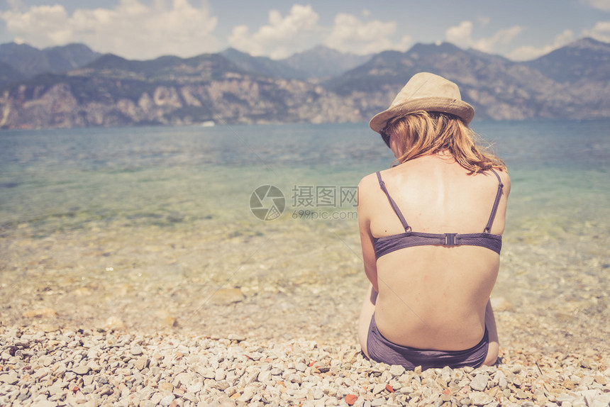 带比基尼的年轻女孩坐在小石头沙滩上意大利图片