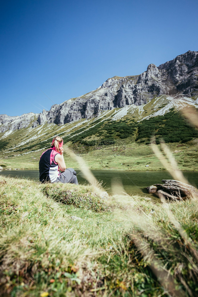 穿运动服的妇女正在徒步时休息坐在地上享受山和湖风景图片