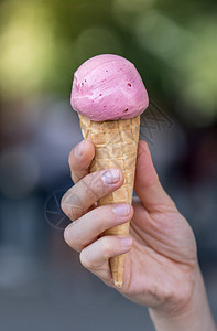 举着冰淇淋女人手里握着草莓冰淇淋阳光明媚的夏日模糊背景背景