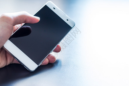 男人手里握着现代智能手机背景是灰色桌子图片