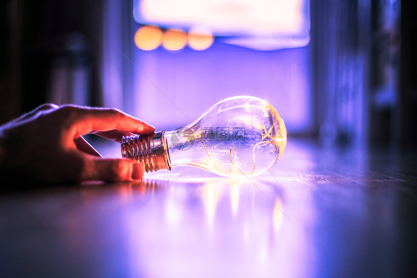 手举着一个LED灯泡在木制地板上是思想和创新的标志在模糊背景中是窗口和灯光图片