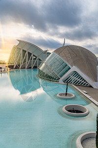 西班牙巴伦亚市科学城的全景电影院游客在城市科学博物馆旁边参观其背景是黎明时有云和太阳背景图片