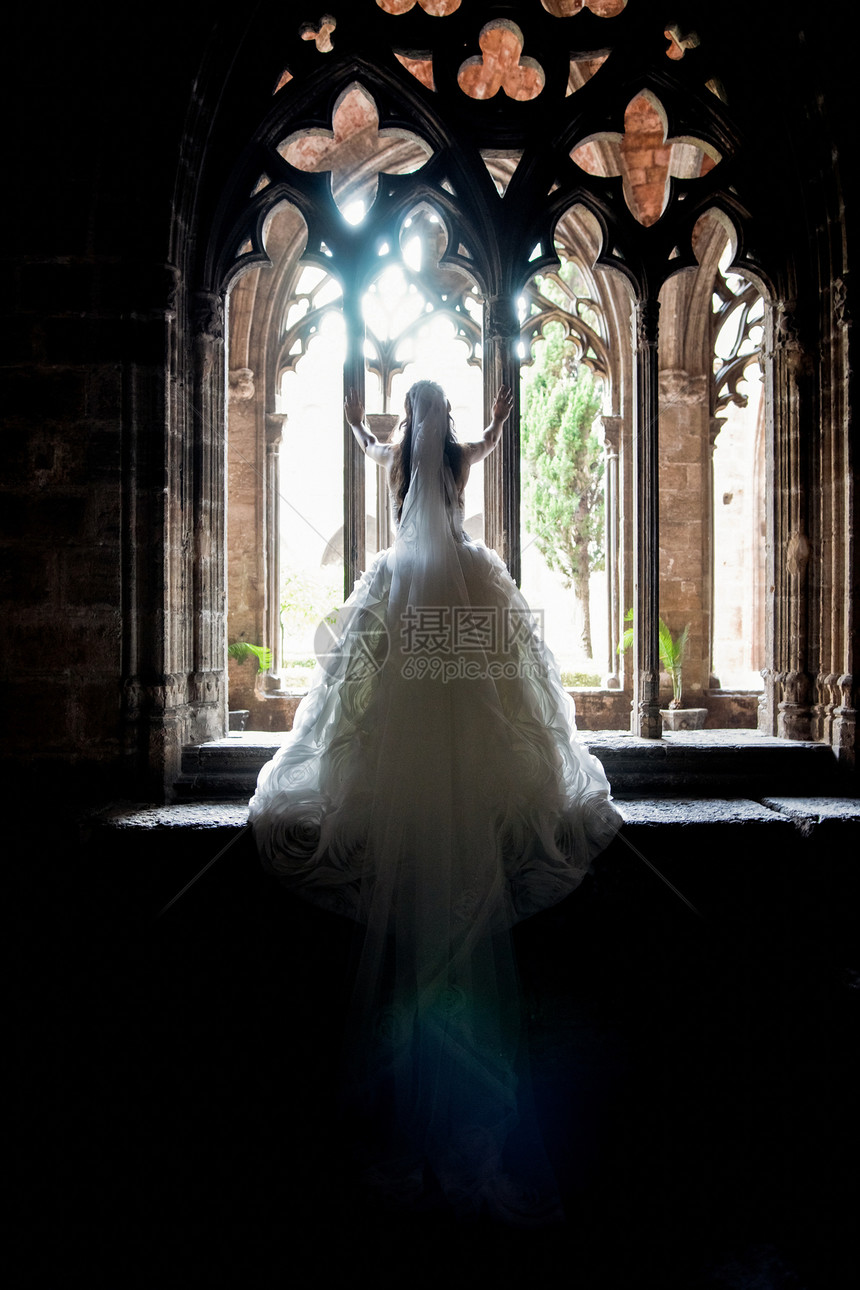 新娘背着她的长尾婚纱在修道院的旧窗户上图片