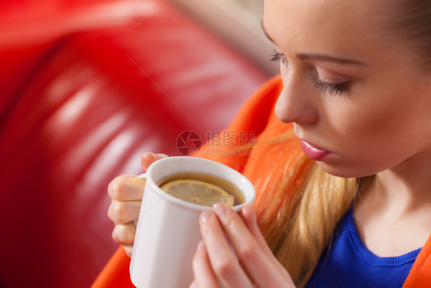 睡在沙发上的年轻女子躺在温暖的毯下喝茶咖啡或不同的热饮图片