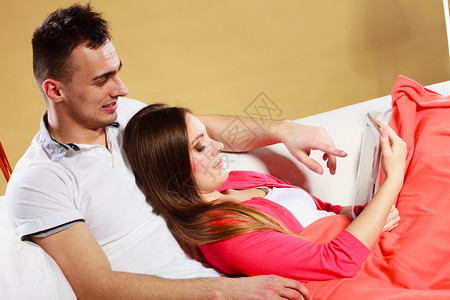 使用平板电脑浏览网络的夫妇使用新技术浏览互联网的男女在家庭沙发上休息图片