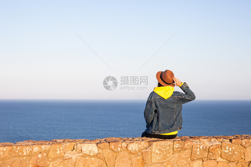 穿旅行服装和戴帽子的妇女坐着看蓝海和天空旅行概念照片坐着和看蓝海天空的妇女图片
