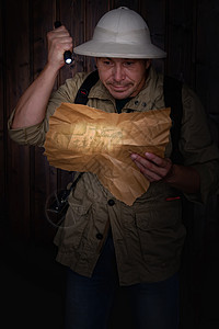 穿着软木头盔和卡其服的旅客看着一张旧显示手电筒的亮点背景图片