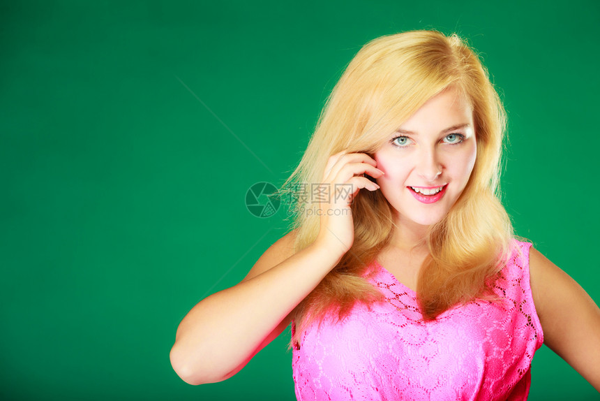 金发型美貌女概念粉红顶部的金发美女紧握着她的脸部绿背景摄影棚拍粉红顶部的笑容金发美女图片
