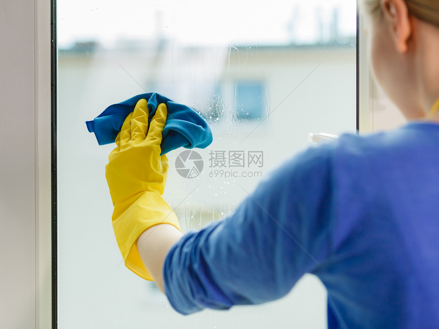 穿黄色手套的年轻女士用蓝色抹布和喷雾洗涤剂擦窗户春季清洁家务概念用洗涤剂擦窗户的女孩在家里用洗涤剂擦窗户图片