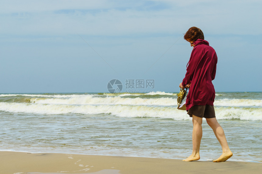 在温暖的秋天气下妇女有闲暇时间在海滩上赤脚徒步行手握鞋凉图片