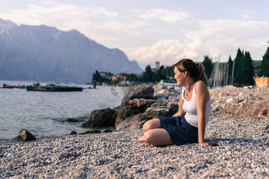 美丽的年轻女士坐在石子沙滩上享受风景度假图片
