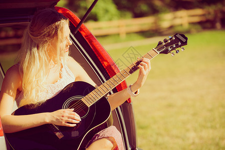 嬉皮士美女坐在露营车后备箱内弹奏吉他图片