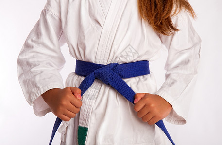 穿着白色传统和服的小女孩在训练或比赛前拉在蓝带上绑空手道带上图片