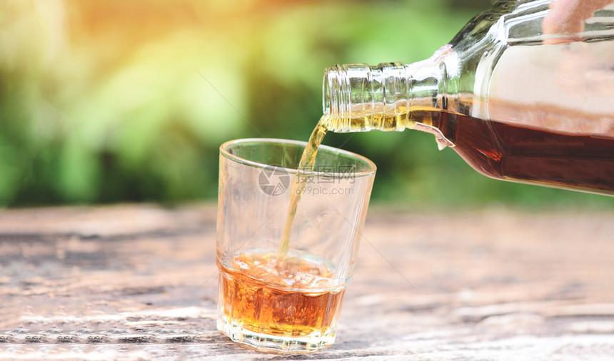 将威士忌或酒精饮料从瓶倒到杯放在木背景酒上图片