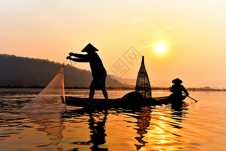 在湄公河中使用木造船抛出净日落或的亚洲渔网具有山地背景生命的Silhouette渔船背景图片