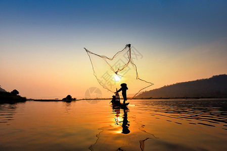 在湄公河中使用木造船抛出净日落或的亚洲渔网具有山地背景生命的Silhouette渔船背景图片