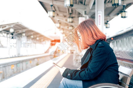 年轻的亚洲女坐在板凳上等待火车并使用手机图片