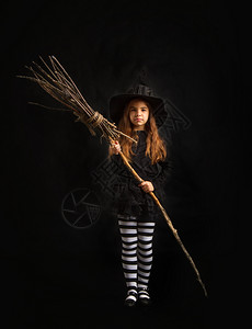 穿着传统的万圣节礼服戴尖帽的小孩站在黑暗背景的木头胡须上图片
