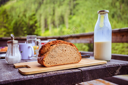 在高山小屋吃早餐的新鲜黑脆面包木板和玻璃瓶里的牛奶图片