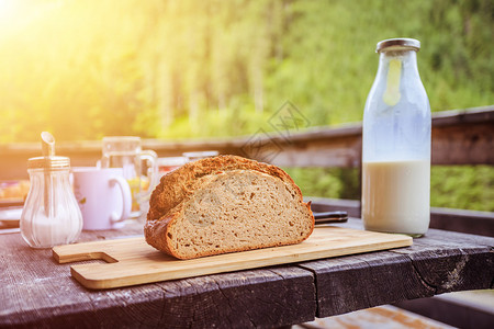 在高山小屋吃早餐的新鲜黑脆面包木板和玻璃瓶的牛奶阳光图片