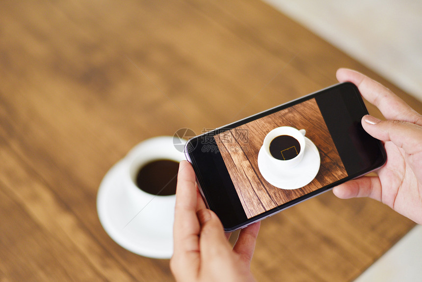 拍摄带相机智能手的照片咖啡杯用于技术上传文件到互联网关闭手持机在木制桌上拍摄咖啡杯的妇女图片