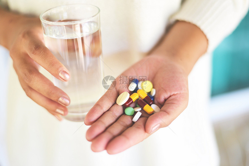 采取医药保健和人的概念手持许多色药片的妇女和带水杯图片