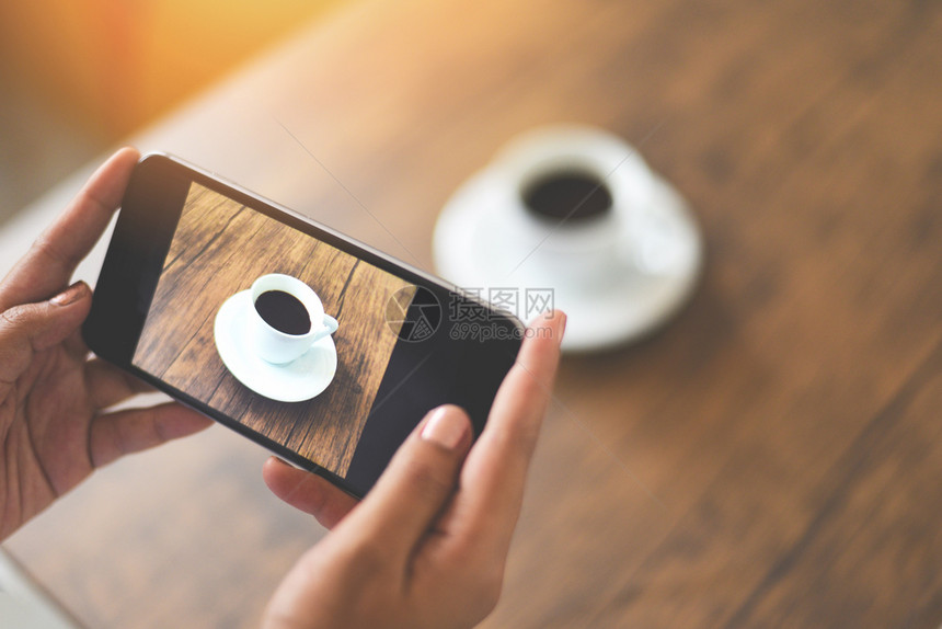 拍摄带相机智能手的照片咖啡杯用于技术上传文件到互联网关闭手持机在木制桌上拍摄咖啡杯的妇女图片