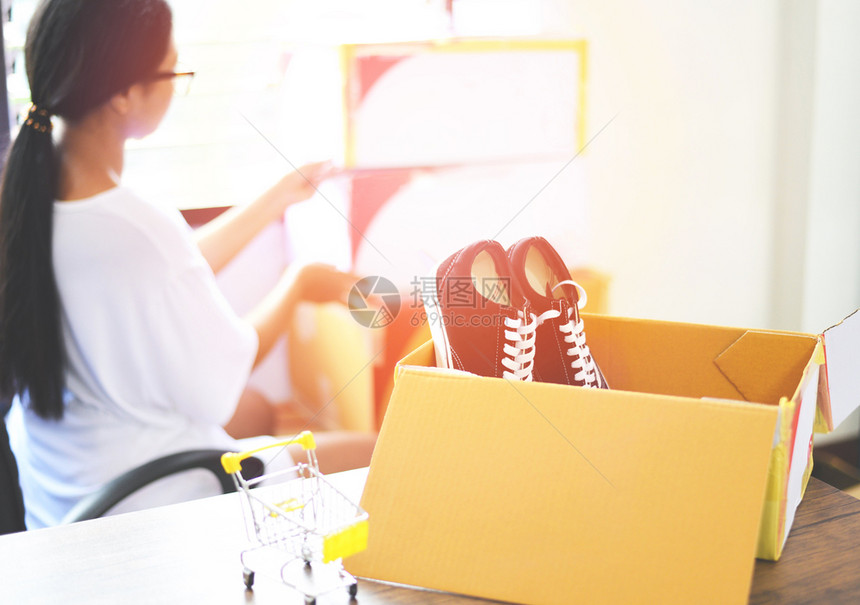 在线销售网上电子商务航运网上购物交货和订启动小企业主工作概念年轻女在纸板箱中包装运动鞋给客户图片