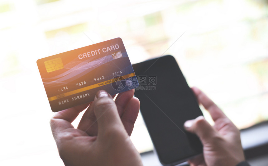 持有信用卡和使智能手机在线购物的妇女手在家中支付技术钱包的网上付款人信用卡模型图片