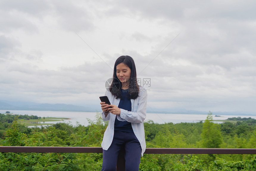 在泰公园旅行和户外度假期间快乐的亚洲妇女使用移动智能手机在热带森林社交媒体上聊天或致电朋友图片