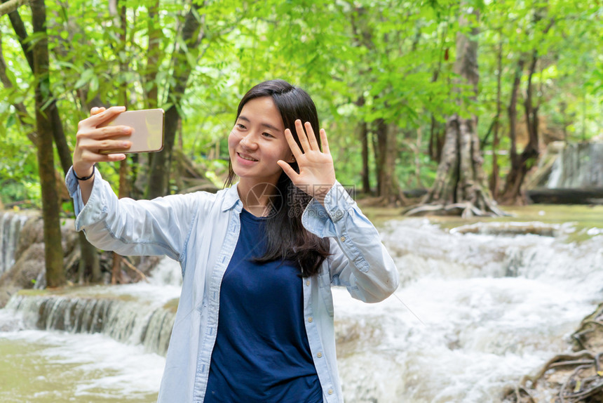 喜悦的亚洲女在热带森林瀑布的社交媒体上自拍图片