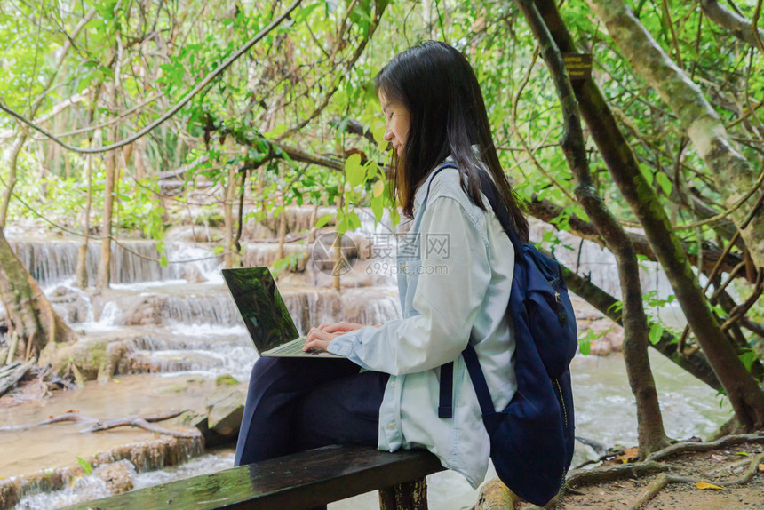 在泰公园旅行和户外度假期间在热带森林瀑布使用笔记本电脑图片