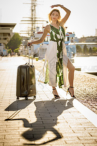 时装女郎抵达新城市美丽的时装模特在到达后将手提箱放在车轮上图片