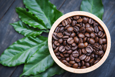 木碗上烤咖啡豆和深底绿色咖啡叶图片