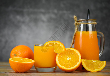 玻璃罐中的橙子汁和木制桌上的新鲜橙子水果片图片