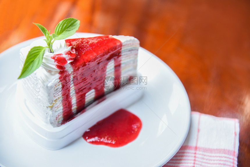 煎饼切片白盘上的草莓酱桌木背景一块蛋糕彩虹和奶油图片