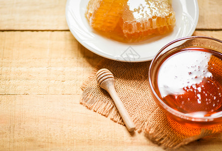 白色蜂蜜罐里新鲜的甜蜜在木制餐桌背景的白板上有木制甜料和蜂窝背景