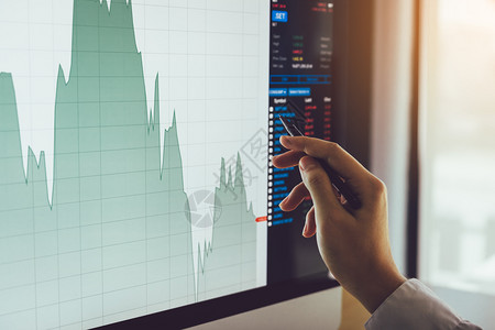 靠近商人的手指向股票市场图和计算机屏幕分析图片