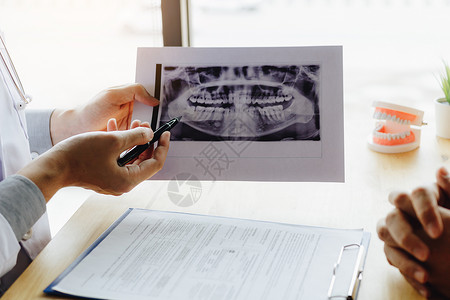 牙科医生手持笔指着X光照片与病人谈论药物和外科治疗图片