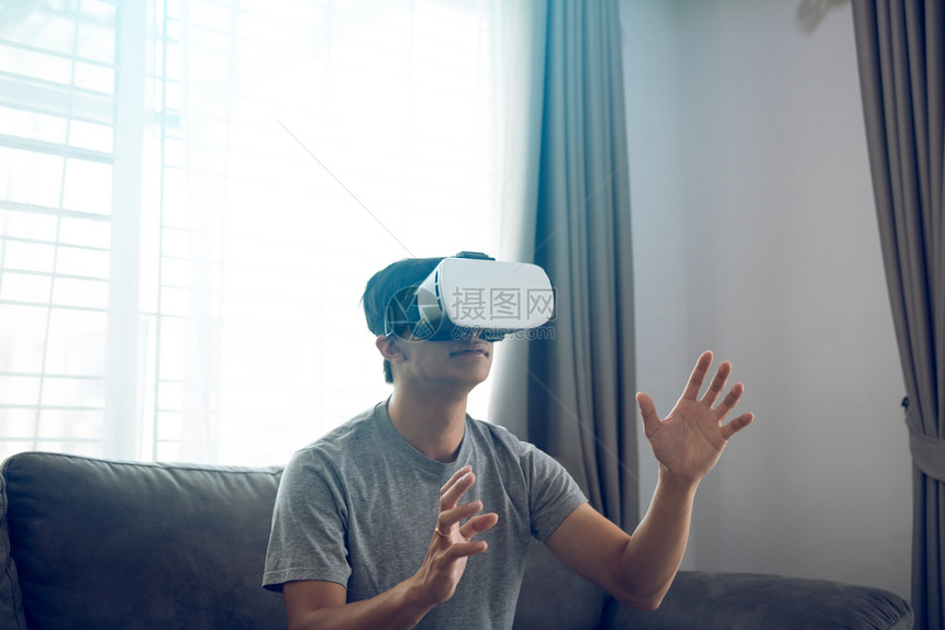 年轻的亚洲男子在客厅戴虚拟现实眼镜以欣赏虚拟现实图片